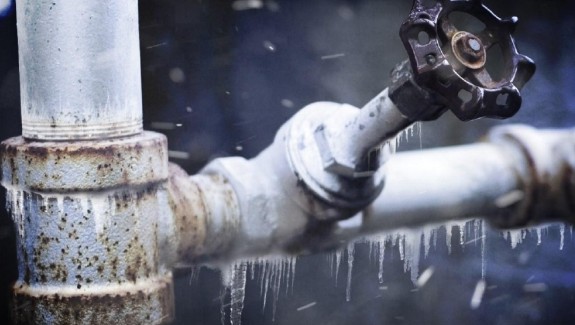 Close-up of a rusted industrial pipe with valve, water droplets visible around it.