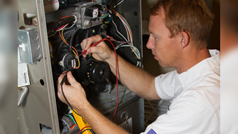 Technician working on an open electrical panel, connecting wires.