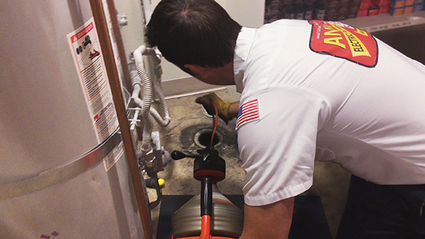 The Holidays Can Strain Your Drains 1 Person in a uniform using drain cleaning equipment near a water heater.