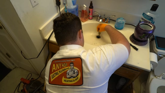 Plumber in a white shirt works on a bathroom sink with tools nearby.