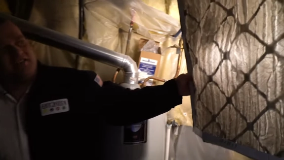 Person in dark clothing inspecting a filter near a water heater in a dimly lit space.