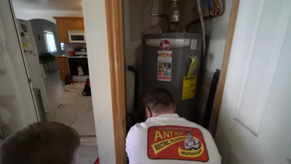 Technician in a red and white uniform working on a water heater inside a home.