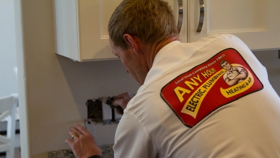Person in a white shirt with a red logo working on an electrical outlet in a kitchen.