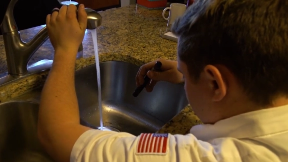 Person testing water flow from a kitchen faucet over a stainless steel sink.