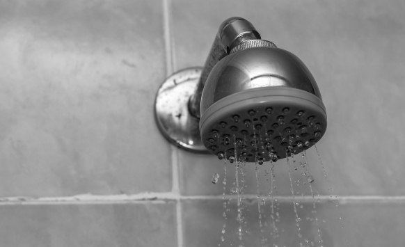A photo of a shower head with water droplets falling.