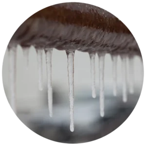 Close-up of icicles hanging from a rusted metal pipe against a blurred background. The image conveys a cold, wintery atmosphere and textural contrast.