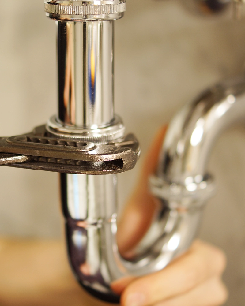 Close-up of a wrench tightening a sink's pipe, hand in background.