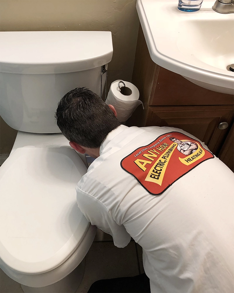 Plumber in a white shirt working on a toilet next to a sink and cabinet.