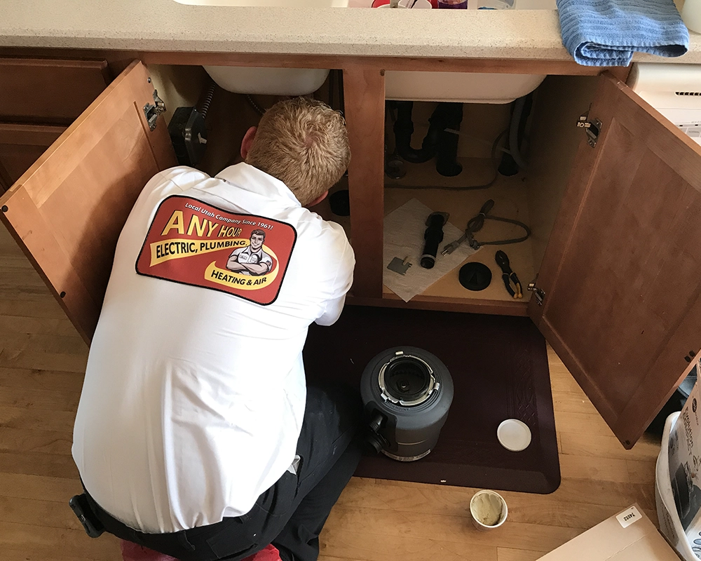 Plumber fixing sink with tools scattered inside open cabinet.